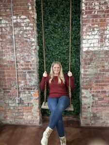 girl sitting on swing in jeans and a red sweater in front of a green ivy brick wall