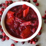 cranberry sauce in a white bowl, whole cranberries and two cinnamon sticks sitting around the white bowl