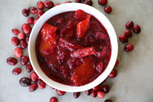 cranberry sauce in a white bowl, whole cranberries and two cinnamon sticks sitting around the white bowl