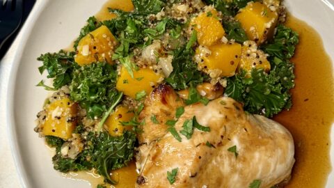 White plate with a baked chicken breast next to a pilaf of butternut squash, kale, and quinoa and a brown sauce underneath.