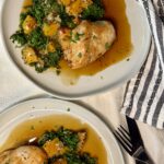 Two white plates with a baked chicken breast next to a pilaf of butternut squash, kale, and quinoa and a brown sauce underneath.