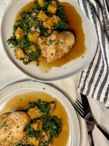 Two white plates with a baked chicken breast next to a pilaf of butternut squash, kale, and quinoa and a brown sauce underneath.