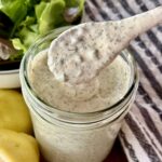 mason jar full of homemade ranch sitting on a wooden board next to fish lemon, chives, and a bowl of lettuce.