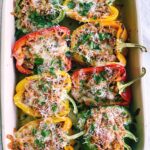 colorful bell peppers cut in half laying in a baking pan. stuffed with sausage mixture and topped with cheese.