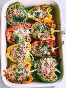 colorful bell peppers cut in half laying in a baking pan. stuffed with sausage mixture and topped with cheese.