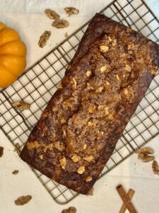 loaf of pumpkin bread sitting on a wire rack with an orange pumpkin in the background