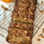 loaf of pumpkin bread sitting on a wire rack with an orange pumpkin in the background