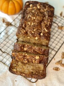 loaf of pumpkin bread sitting on a wire rack with an orange pumpkin in the background