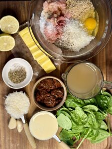 bowl of ground chicken with an egg, pinko, cheese and seasonings. sliced butter, broth, tomatoes, cream, spinach, lemon, and cheese on top of wooden board