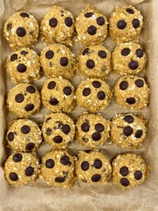 unbaked pumpkin oatmeal chocolate chip cookie dough balls lined up on brown parchment paper.