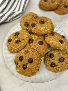 baked pumpkin oatmeal chocolate chip cookies piled on a grey scalloped plate with two cookies in the background