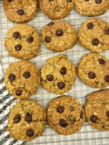 baked pumpkin oatmeal pumpkin chocolate chip cookies on top of a wire cooling rack next to a grey and white stripped towel