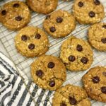 baked pumpkin oatmeal pumpkin chocolate chip cookies on top of a wire cooling rack next to a grey and white stripped towel