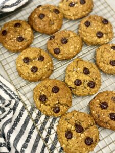 baked pumpkin oatmeal pumpkin chocolate chip cookies on top of a wire cooling rack next to a grey and white stripped towel