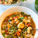 white bowls full of minestrone soup with grey background