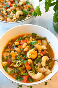 white bowls full of minestrone soup with grey background