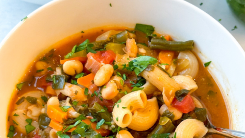 white bowls full of minestrone soup with grey background