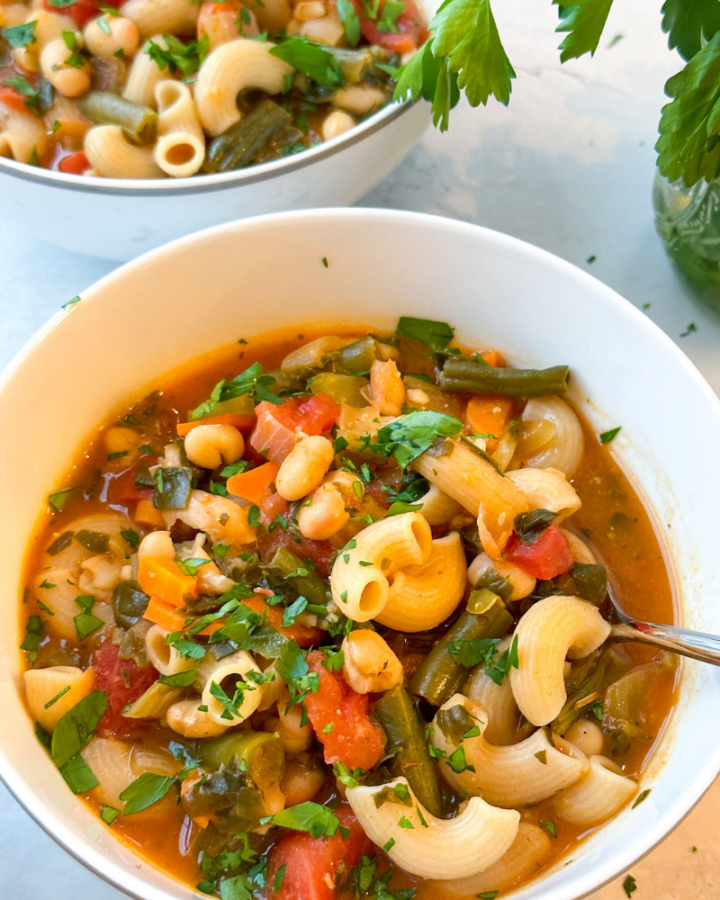 white bowls full of minestrone soup with grey background