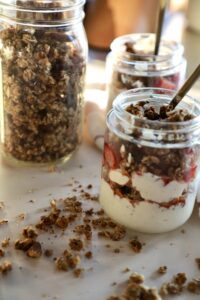 three glass jars: one with homemade granola and the other two filled with yogurt, granola, and strawberries.