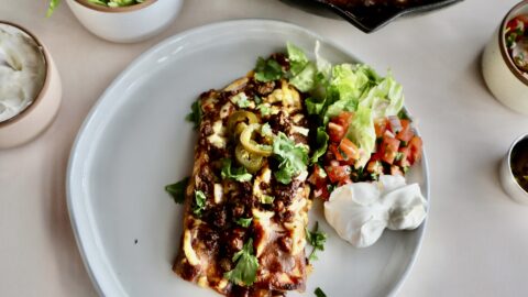 Easy ground beef enchiladas in a cast iron pan, two enchiladas on a plate, and a bowl of lettuce.